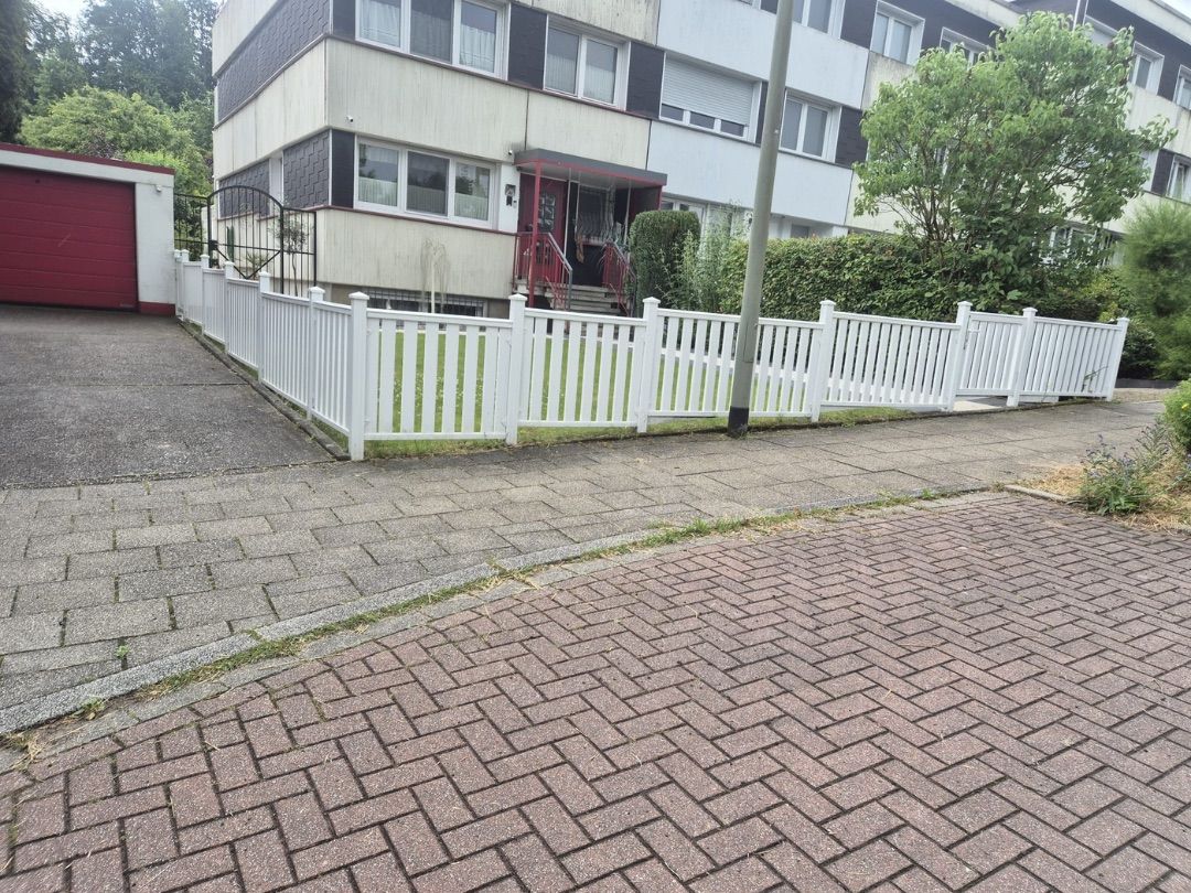 Weißer Gartenzaun mit Lattenoptik als Vorgarteneinfassung an einem Wohnhaus