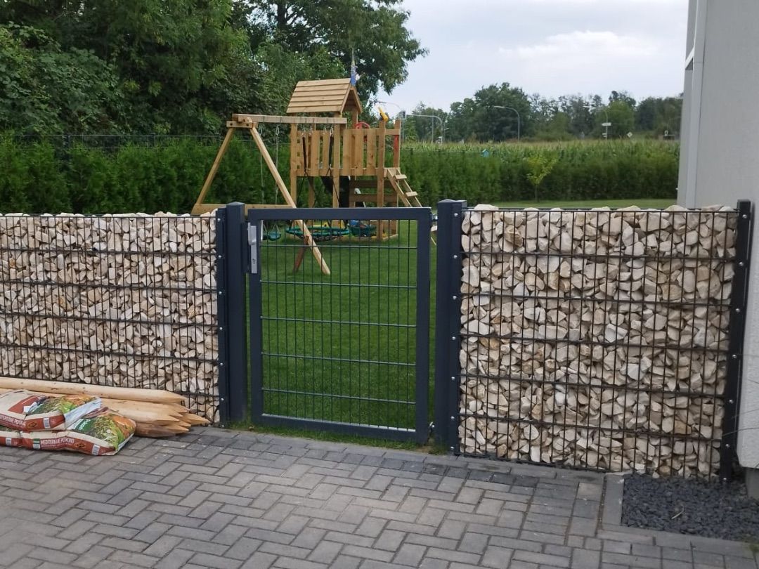 Gabionenzaun mit Natursteinfüllung und anthrazitfarbenem Gartentor
